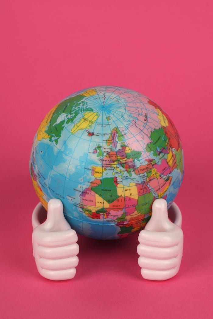 Vibrant globe figurine held by hands on a pink backdrop, symbolizing travel and global unity.