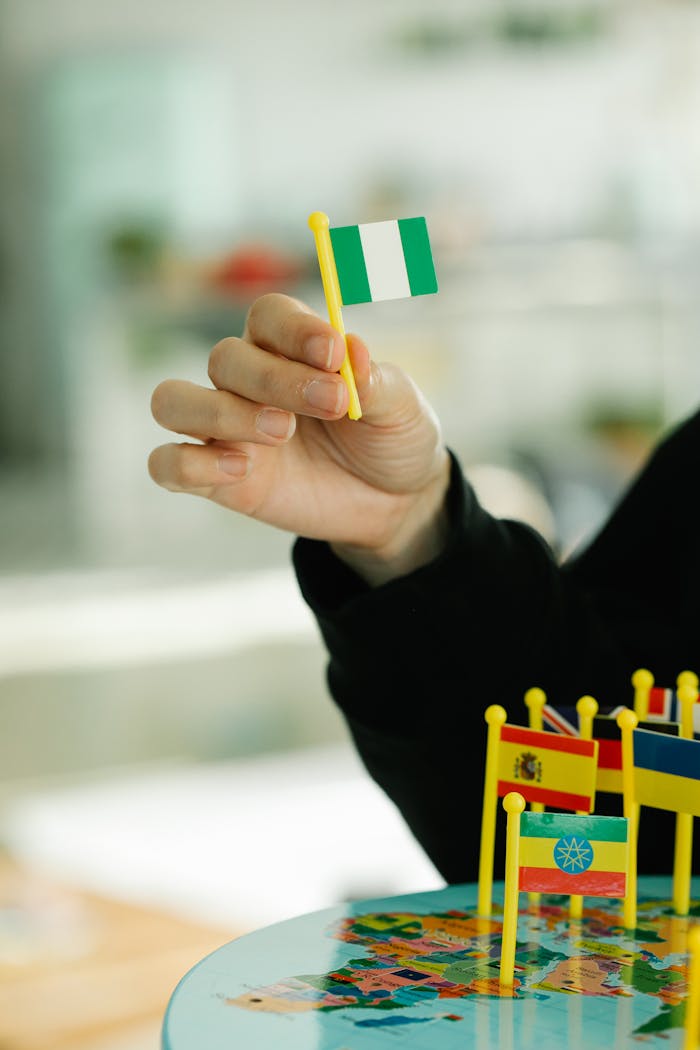 A close-up of a hand holding a small Nigerian flag, focusing on world geography.